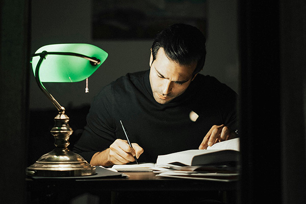 Man writing at a desk with a lamp - Photo by Dziana Hasanbekava from Pexels